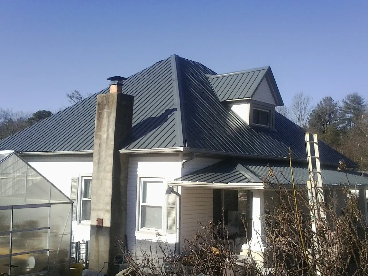 Dark blue standing seam metal roof on a white farmhouse with dormer — Slate & Tile Roof Repair by Roofing Brothers in Bowling Green