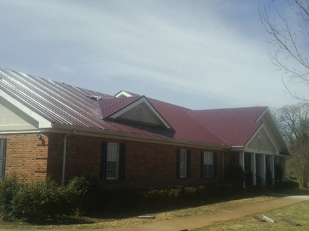 Red metal roof with gabled entries on a long brick building, from a Hail Damage Roof Repair job in Bowling Green