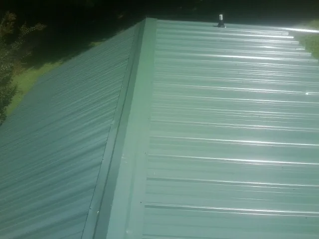 New green metal panels meeting at the ridge of a roof — Flat Roof Repair work by our crew in Bowling Green